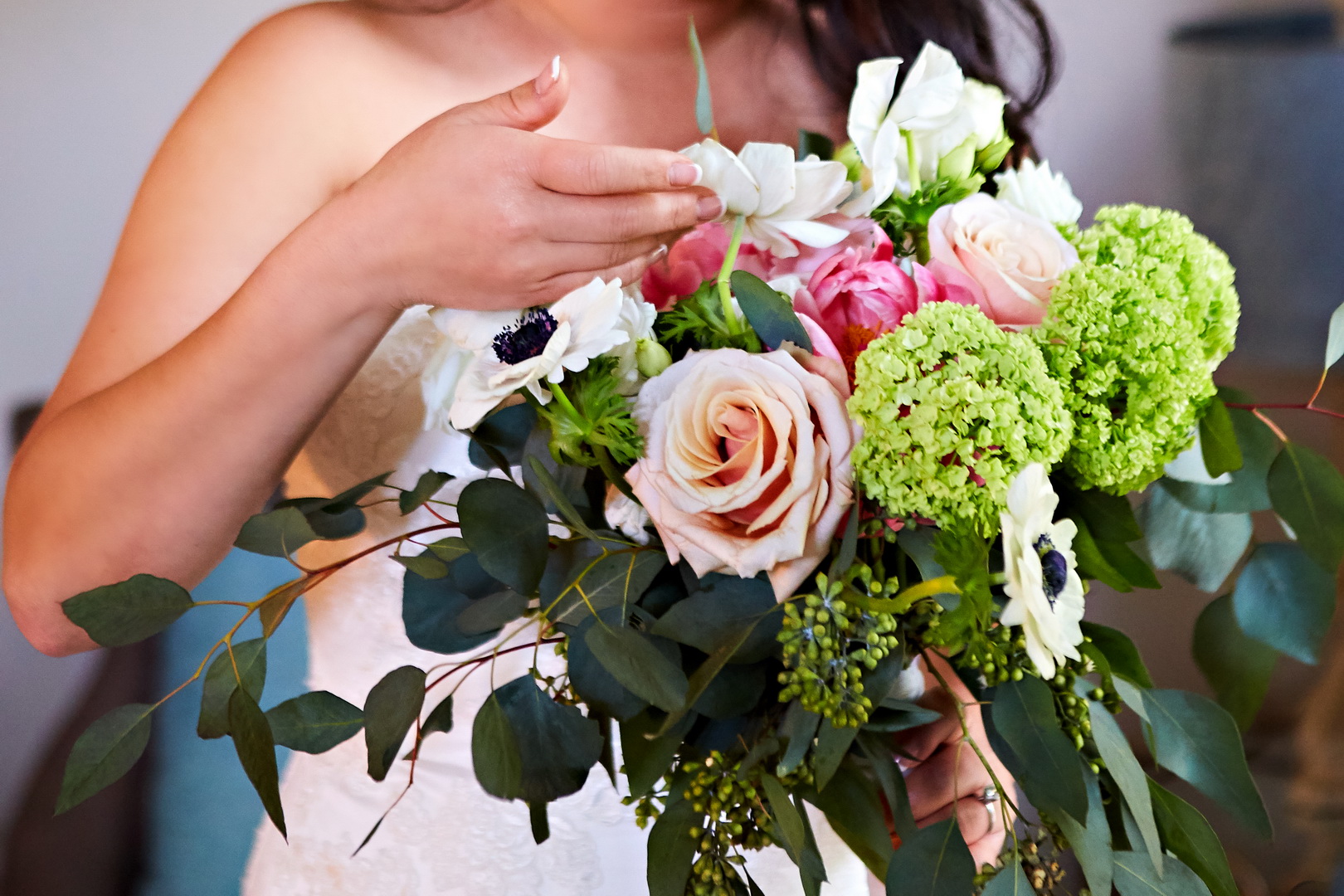 Close up detail of bride looking at bouquet of roses, anemones, and peonies.