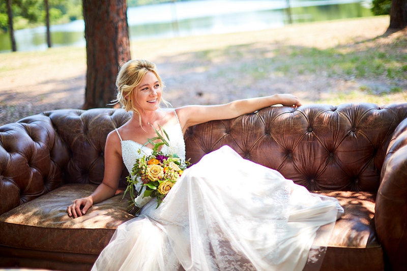 Smiling Bride lounging on brown couch with colorful bouquet at Charleston Woodlands