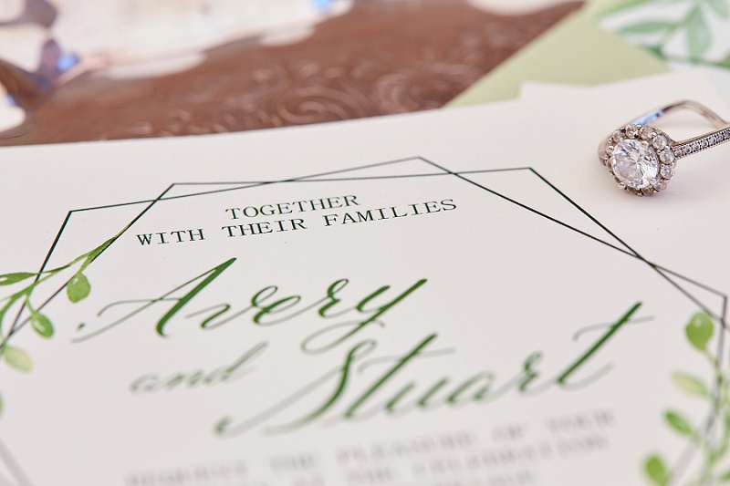 Close up of engagement ring and green wedding invitation suite