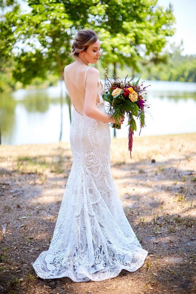 Charleston bride stands in lace wedding dress, looking down at her colorful bouquet, while at Charleston Woodlands