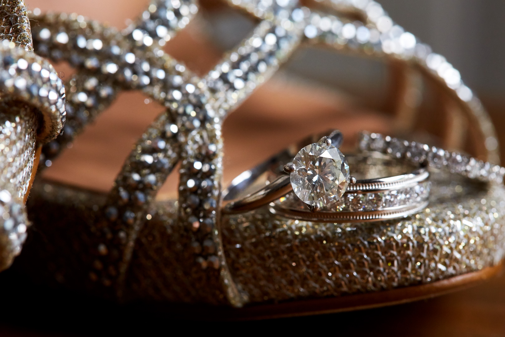 Close up of diamond engagement ring and wedding bands on toe of jeweled shoe of bride