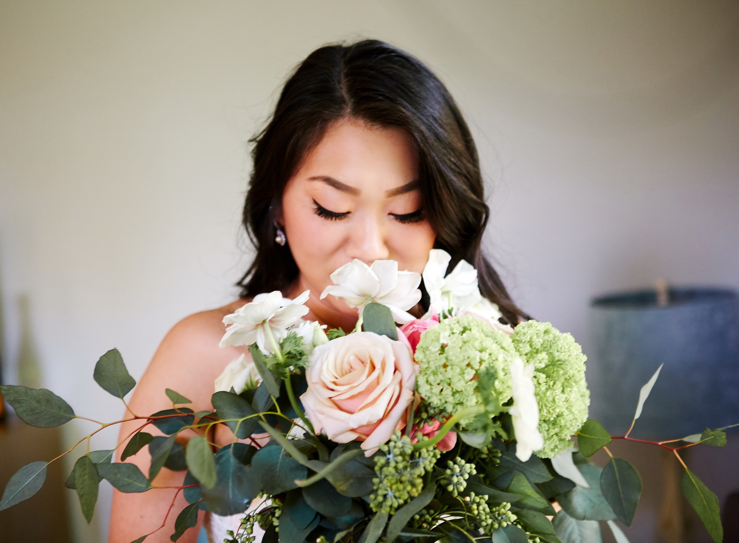 Bride smelling her bouquet of roses, anemones, and peonies.