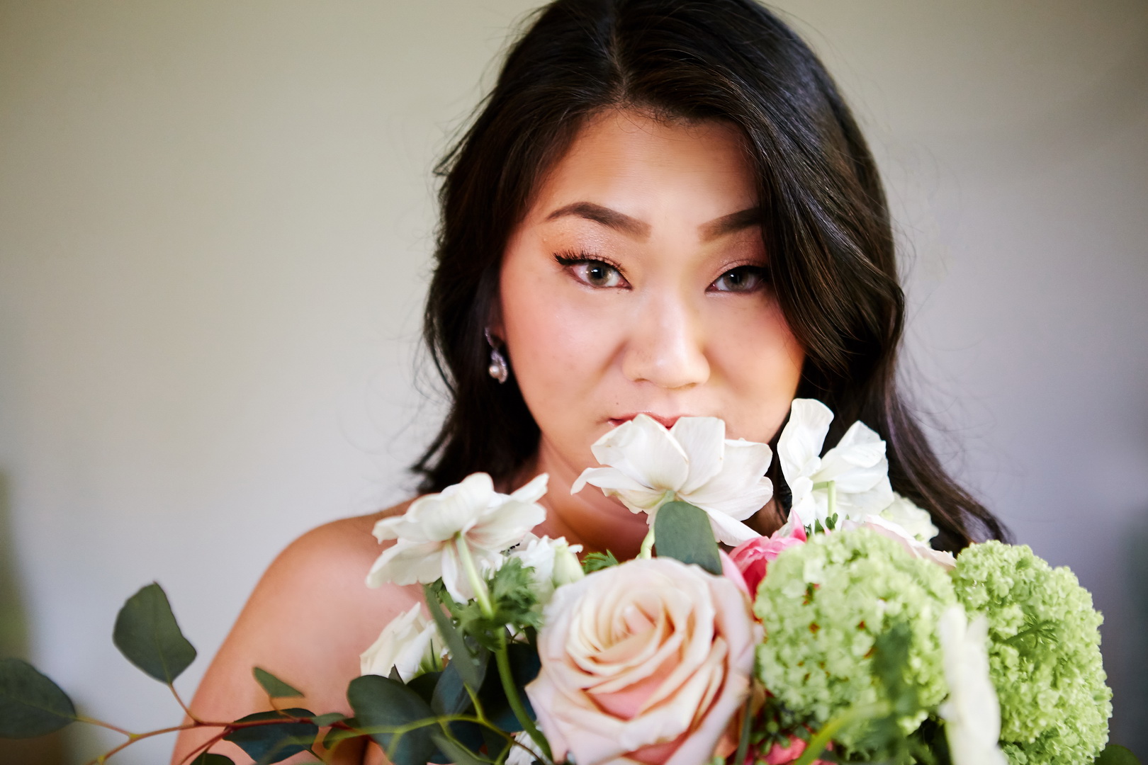Close up portrait of the bride with bouquet of roses, peonies, and anemones.
