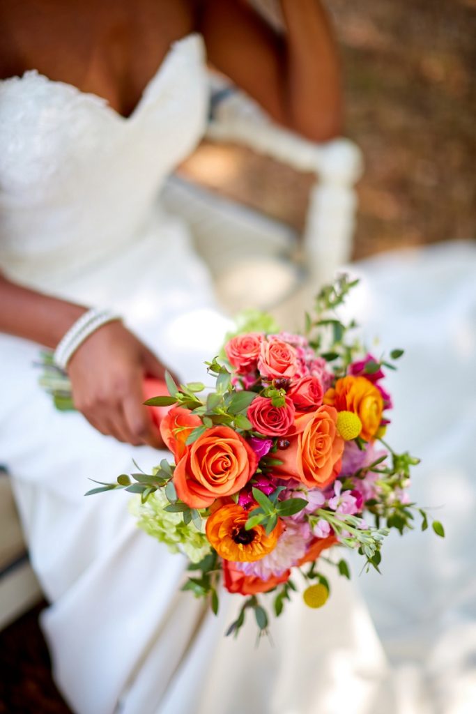 Detail of bride wedding dress, bracelet, and colorful orange and pink bouquet