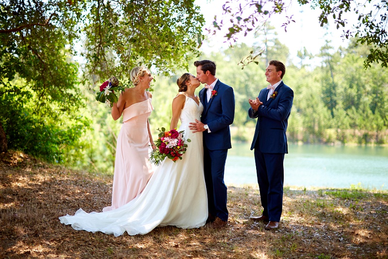 Maid of honor and best man look on while bride and groom kiss at ceremony arbor in Charleston Woodlands