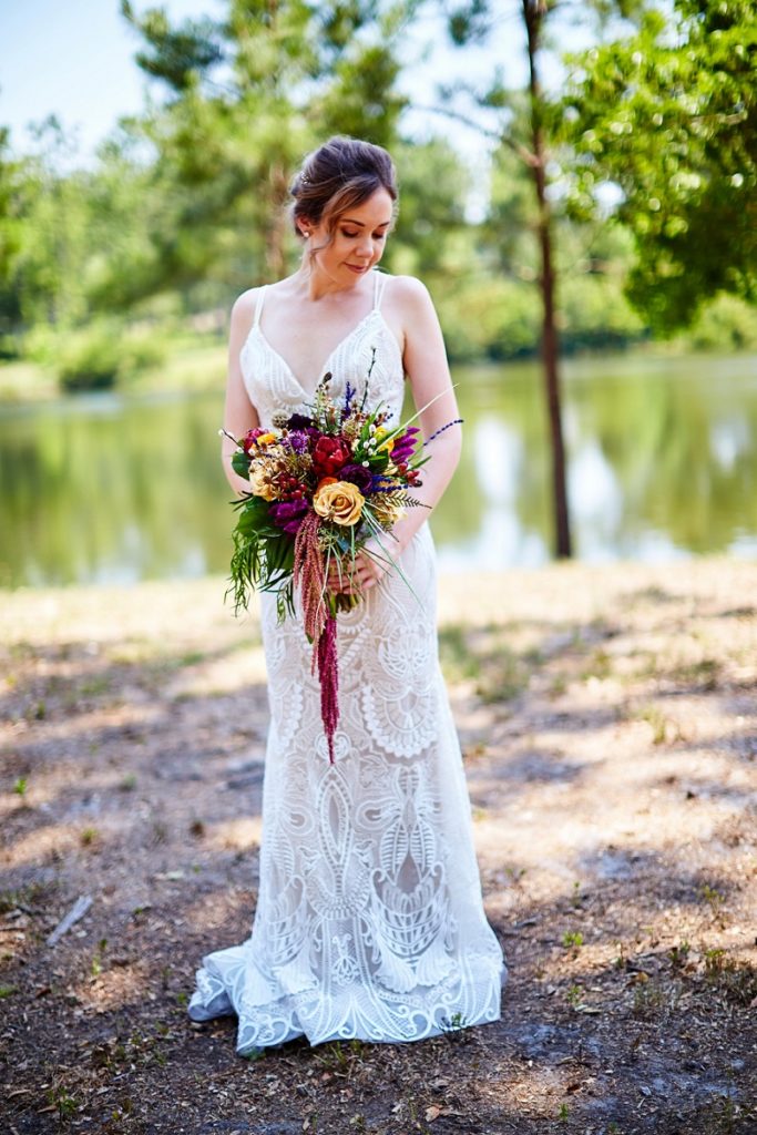 Bride in lace wedding dress looking at colorful bouquet at Charleston Woodlands