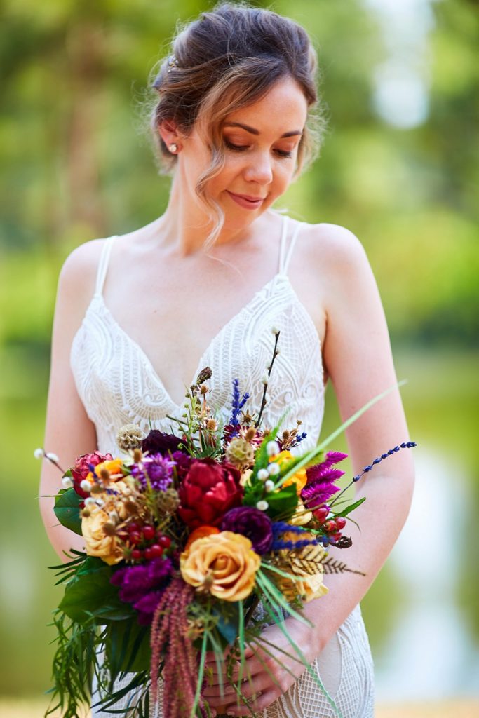 Bride in lace dress looking down at colorful bouquet
