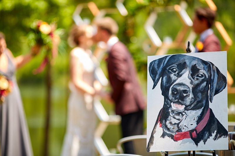 Painting of dog with bride and groom kissing in the out of focus background