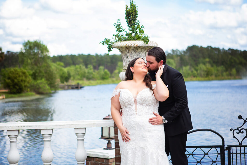 Portrait of groom standing behind bride, kissing her cheek, in front of a lake at Eden at Gracefield in Walterboro, SC - photographed by Charleston wedding photographer Luxe By Lindsay Photography