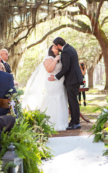 Bride and groom share their first kiss as a married couple at their wedding ceremony with oak trees in the background at Eden at Gracefield  - photographed by Charleston wedding photographer Luxe By Lindsay Photography