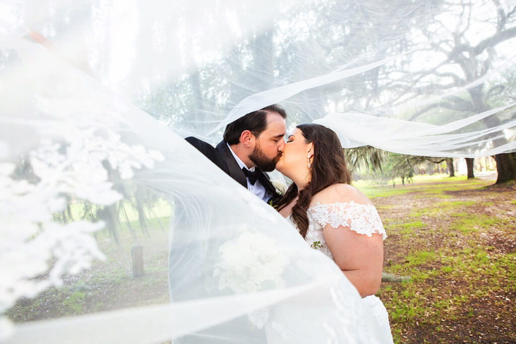 Bride and groom kiss with bride's long veil surrounding them - photographed by Charleston wedding photographer Luxe By Lindsay Photography