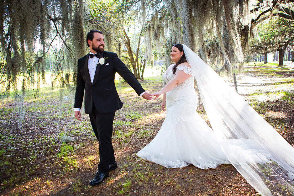 bride and groom hold hands as the groom leads the bride om a walk through the trees at Eden at Gracefield - photographed by Charleston wedding photographer Luxe By Lindsay Photography