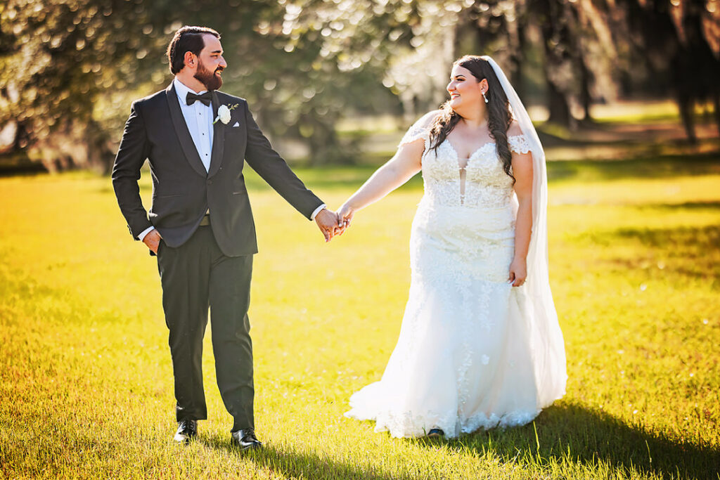 Bride and groom look at each other while holding hands and walking on the lawn during golden hour at Eden at Gracefield - photographed by Charleston wedding photographer Luxe By Lindsay Photography