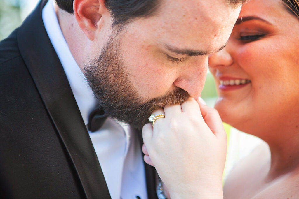 Close up of bride smiling while groom kisses her left hand, showing her engagement ring and wedding band - photographed by Charleston wedding photographer Luxe By Lindsay Photography