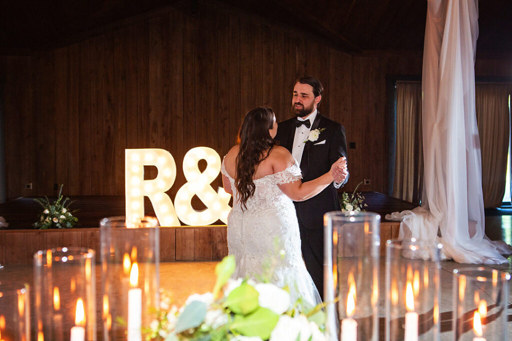 Bride and groom dance together in candlelit barn reception hall with their lit initals in the background and candles in the foreground - photographed by Charleston wedding photographer Luxe By Lindsay Photography