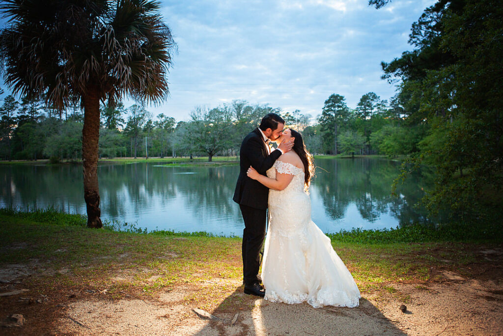 Bride and groom kiss at dusk while in front of a lake and palmetto and oak trees at Eden at Gracefield - photographed by Charleston wedding photographer Luxe By Lindsay Photography