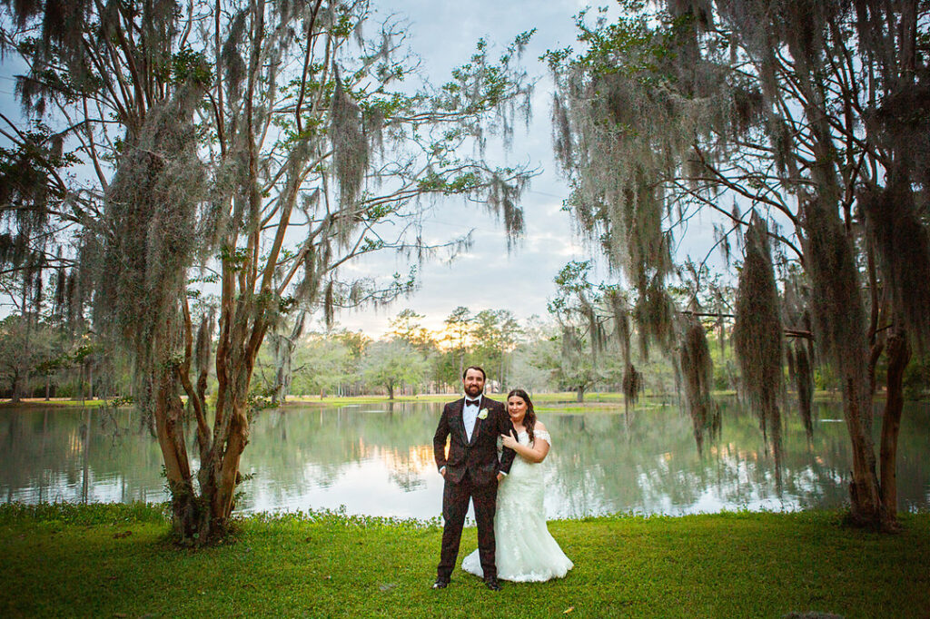 Bride and groom smiling portrait in front of the lake and trees at sunset at Eden at Gracefield - photographed by Charleston wedding photographer Luxe By Lindsay Photography