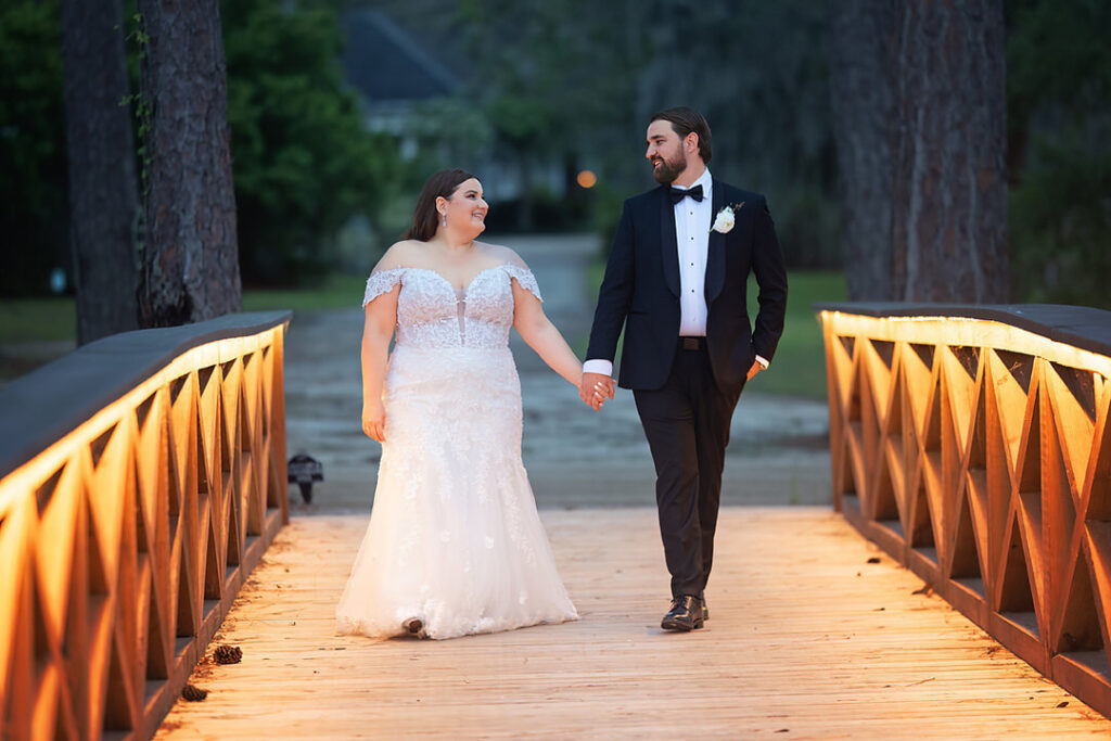 Bride and groom walk across the lit up bridge while looking at each other at Eden at Gracefield - photographed by Charleston wedding photographer Luxe By Lindsay Photography